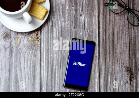 Un telefono cellulare o cellulare su un tavolo di legno Con l'app Jet Blue aperta accanto a un caffè e bicchieri Foto Stock