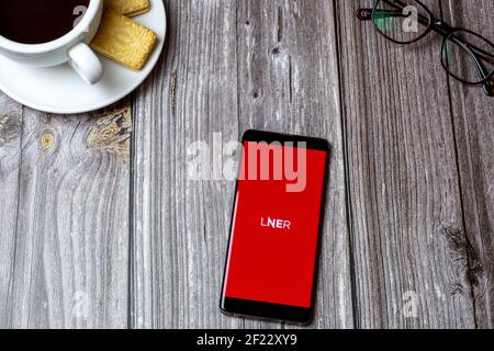 Un telefono cellulare o cellulare su un tavolo di legno Con l'app LNER aperta accanto a un caffè e. occhiali Foto Stock