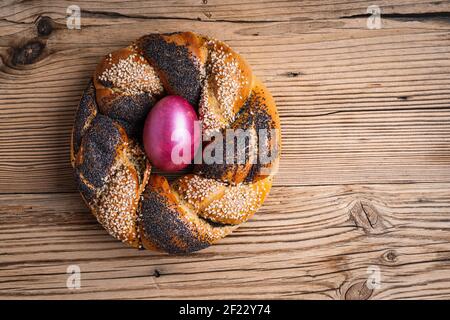 Anello di pane pasquale fatto in casa decorato con semi di sesamo papavero, uovo viola tinto naturale su rustico sfondo di legno, vista dall'alto Foto Stock