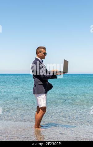 Uomo d'affari che usa un computer portatile sulla spiaggia tropicale. Concetto di vacanza estiva. Foto Stock