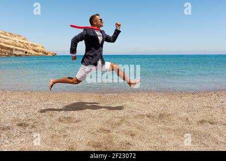 Felice uomo d'affari che corre via dal lavoro d'ufficio sulla spiaggia. Concetto di vacanza estiva. Foto Stock