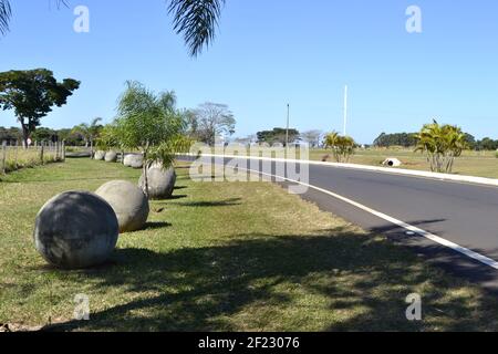 Strada. Strada asfaltata all'interno del Brasile, Sud America, con manufatti in cemento in mostra accanto alla strada ondulata con una torre sullo sfondo, Foto Stock