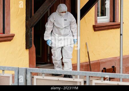 Weilerbach, Germania. 10 marzo 2021. Un dipendente del dipartimento di medicina legale esce da una casa residenziale in una proprietà all'ingresso del villaggio. Dopo la scoperta di due corpi in una casa a Weilerbach vicino Kaiserslautern, la polizia continua a cercare un sospetto a piena velocità. Credit: Uwe Anspach/dpa/Alamy Live News Foto Stock