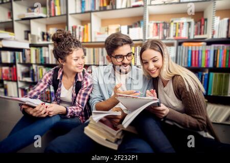 Tre giovani allegri amici universitari seduti sul divano della biblioteca pronti per l'esame. Foto Stock