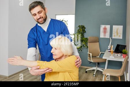 Donna anziana con lesione ad un giunto a gomito. Dolore articolare. Il fisioterapista tiene la mano di una donna durante la riabilitazione Foto Stock