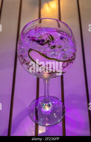 Cocktail fresco con cetriolo in un bicchiere di vino con luce al neon. Festa d'estate di fondo. Foto Stock