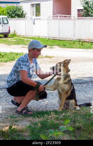 Un cucciolo di cane di Pastore tedesco dà una zampa ad a. ragazzo adolescente su una strada rurale in un giorno d'estate Foto Stock