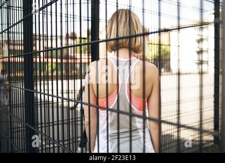 Vista posteriore della donna bionda che guarda i bambini che giocano in un campo da basket. Stile di vita all'aperto, concetto ricreativo Foto Stock