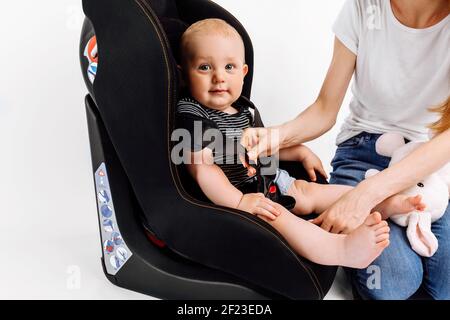 La mamma tinda il suo bambino nel seggiolino per auto, il bambino nel seggiolino per auto, su uno sfondo bianco isolato Foto Stock