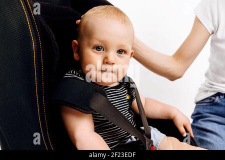 La mamma tinda il suo bambino nel seggiolino per auto, il bambino nel seggiolino per auto, su uno sfondo bianco isolato Foto Stock