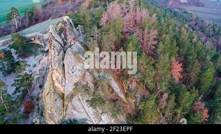 06 marzo 2021, Sassonia-Anhalt, Timmenrode: Un escursionista in una giacca rossa si trova sull'Hamburger Wappen. (Foto scattata con un drone) la formazione di arenaria fa parte di un popolare sentiero di cresta che si snoda dal Großvaterfelsen vicino Blankenburg al Hamburger Wappen vicino Timmenrode. Passando da rocce a forma di bizarvia con nomi fantasiosi come Schweinekopf (testa di maiale), Zwergenhöhe (altezza di nani) o Teufelskessel (cavoldrone del diavolo), lungo il tragitto si gode sempre di una vista impressionante sui mondi montani dell'Harz. La parte del sentiero del crinale nella zona del Muro del Diavolo, conosciuto anche come Th Foto Stock