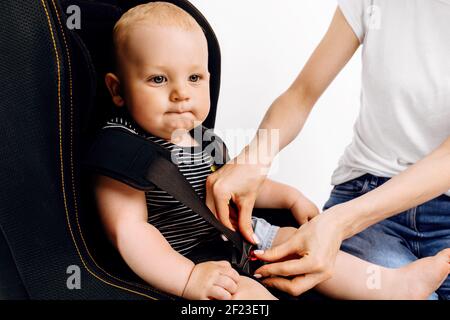 La mamma tinda il suo bambino nel seggiolino per auto, il bambino nel seggiolino per auto, su uno sfondo bianco isolato Foto Stock