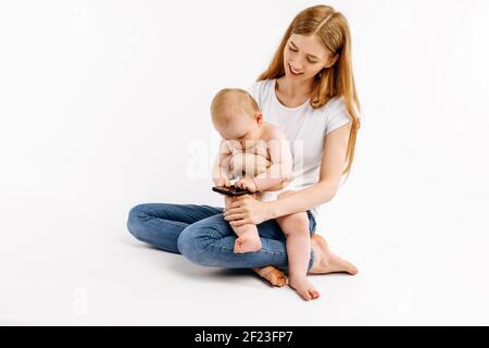 Madre felice e bambino usando il telefono cellulare che gioca insieme seduto su uno spazio di copia isolato su sfondo bianco Foto Stock