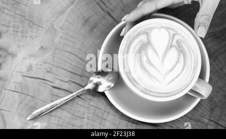 Disegno sulla superficie del latte. Sfida per l'artista latte. Vista dall'alto della tazza da caffè sul tavolo in legno. Bellissimo motivo cuore creato da microschiuma. Caffetteria e caffetteria. Cappuccino a mani femminili. Foto Stock