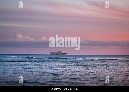 Nave da crociera che si muove all'orizzonte al tramonto sulla spiaggia di Waikiki a Honolulu, Hawaii. Foto Stock