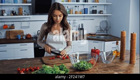 giovane donna in grembiule che taglia i pomodori ciliegini sul tagliere Foto Stock