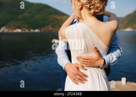 La sposa e lo sposo si abbracciano sul molo di Perast, lo sposo ha messo le mani sulla vita della sposa Foto Stock