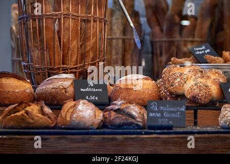 Vario assortimento di pane artigianale nella finestra di una panetteria cittadina con prezzi e nomi in lingua catalana. Foto Stock