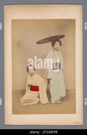 Portret van twee Japanse jonge vrouwen.One delle donne si siede sul pavimento e ha uno slipper nella sua mano sinistra, l'altra donna si alza e ha un parasolo in mano Foto Stock