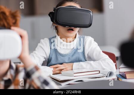 emozionata studentessa in vir cuffia vicino compagno di classe in primo piano offuscato Foto Stock