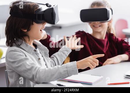 allieva emozionato a toccare il compagno di classe e a puntare con le dita durante il gioco nel visore vr Foto Stock