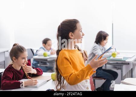 Sorridi ragazzino che tiene il notebook durante la lezione in classe Foto Stock