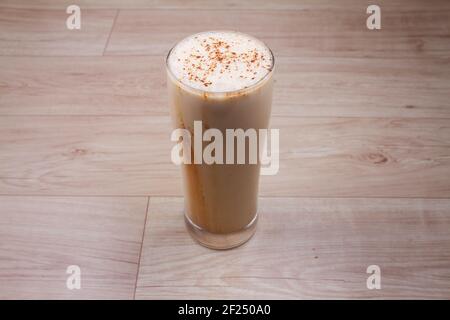 Caffè freddo frullato frullato in un bicchiere con chicchi di caffè su un rustico tavolo di legno con spazio per la copia. Foto Stock
