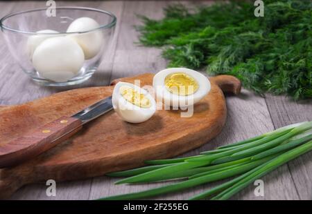 Uova bollite preparate per il taglio su un vecchio tagliere di legno. Ingrediente per le insalate. Concetto di cibo fatto in casa. Cibo naturale. Foto Stock