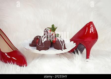 Fragole ricoperte di cioccolato su piatto a piedistallo su pelliccia bianca con pompe rosse Foto Stock