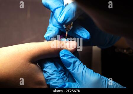 manicure in guanti blu fa una manicure hardware, lavorazione meccanica di unghie con una taglierina, rimozione cuticola con un apparecchio, mani professionale Foto Stock