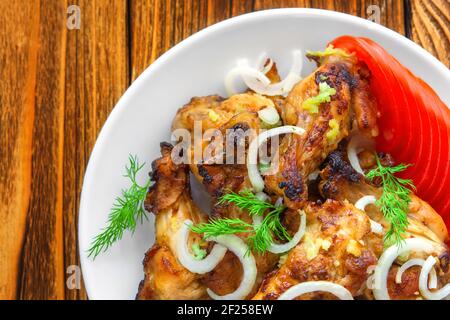 Primo piano con ali di pollo fritte, pomodori freschi, cipolle, aneto, aglio su sfondo di legno. Vista dall'alto. Il concetto di cibo a base di carne. Foto Stock