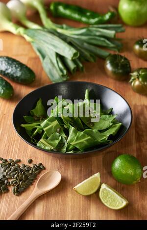 Insalata di spinaci con semi, lime, pomodoro, pepe, cipolla, cetriolo e mela, su un tavolo da cucina in legno. Strumenti di cottura in background. Tagliere. O Foto Stock