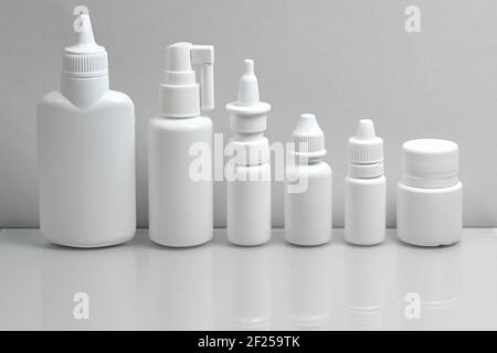 Foto monocromatica a colori grigio. Un set di flaconi bianchi in plastica medica, che mostrano una varietà di forme medicinali, su sfondo grigio. Foto Stock