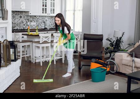 Giovane donna in grembiule verde lavando pavimento con mop Foto Stock
