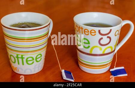 Due tazze di caffè con testo colorato riempito di tè su un tavolo di legno. Foto Stock