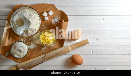 Un set di ingredienti per la cottura di prodotti dolciari a base di farina, burro e uova. Posa di carta marrone su un piano di legno bianco. Foto Stock