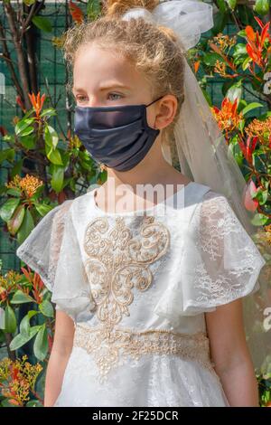 Bella modella ragazza in una maschera protettiva in giardino. Primo piano di una ragazza che indossa un abito principessa con maschera protettiva nera. Stile di bellezza durante la quarantena del focolaio di coronavirus. Foto Stock