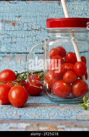 piccoli pomodori freschi accanto a un bicchiere riempito con pomodori di fronte a un muro di legno blu Foto Stock