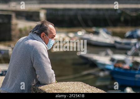 L'aumento del terreno dovuto al bradisismo, fenomeno sismico tipico dei campi Flegrei, e la bassa marea che colpisce varie parti della penisola, ha quasi prosciugato il molo dei pescatori di Pozzuoli (Napoli), un uomo che indossa una maschera guarda il fenomeno dal molo. Foto Stock