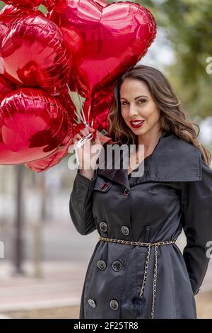 La splendida Brunette ispanica celebra il giorno di San Valentino con una dozzina Palloncini con cuore rosso Foto Stock