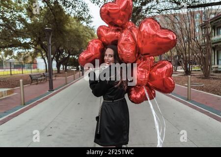 La splendida Brunette ispanica celebra il giorno di San Valentino con una dozzina Palloncini con cuore rosso Foto Stock