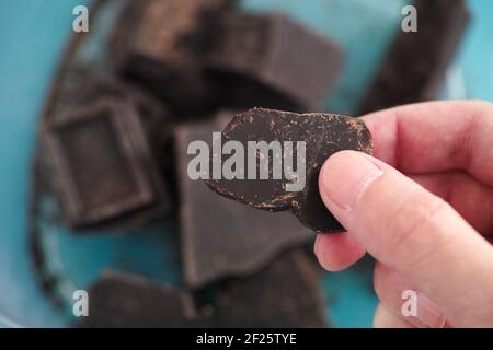 Un uomo che tiene in mano un pezzo di cioccolato fondente rotto in casa. Primo piano. Foto Stock