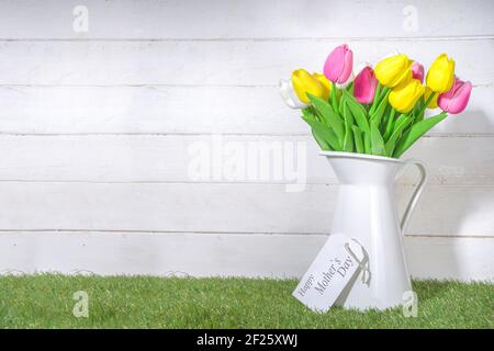 Biglietto d'auguri per il giorno della mamma. Tulipani bouquet in vaso e cartellino di saluto su legno bianco e legno plank sfondo spazio copia Foto Stock