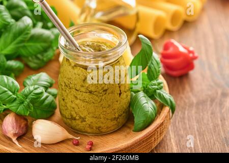 Vasetto con salsa di pesto fatta in casa su fondo rustico con parmigiano, olio d'oliva, pesto di sause, basilico e aglio. Copia sfondo spazio. Foto Stock