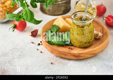 Vasetto con salsa di pesto fatta in casa su fondo rustico con parmigiano, olio d'oliva, pesto di sause, basilico e aglio. Copia sfondo spazio. Foto Stock