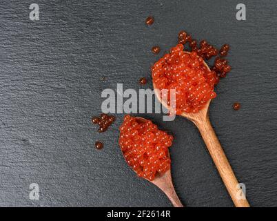 Caviale fresco di salmone al chum rosso granato in cucchiaio di legno, fondo nero, primo piano Foto Stock