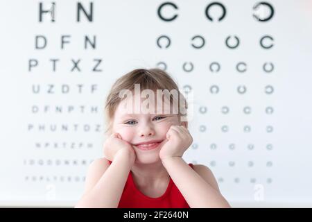 Sorridente bambino contro la tavola di prova della vista in clinica medica verticale Foto Stock