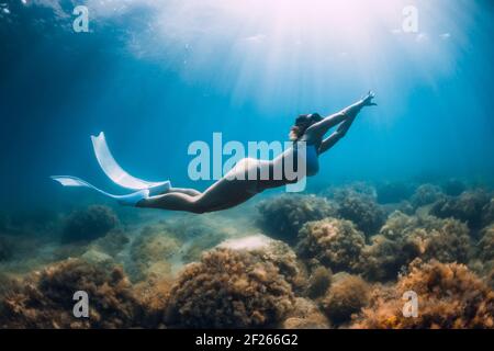 Il freediver scivola su un mare sabbioso con pinne bianche. Donna sottile libera subacquea in blu oceano Foto Stock