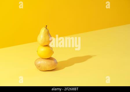 Concetto minimal con patata, limone e pera accatastati su uno sfondo giallo in luce intensa. Immagine monotona gialla con verdure e frutta. Foto Stock