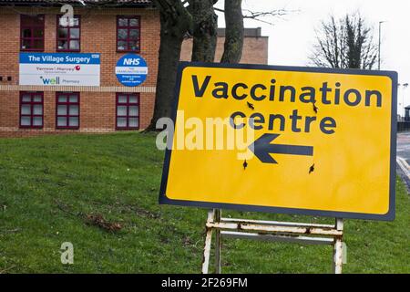 Segno del centro di vaccinazione durante la pandemia di Coronavirus del 2020-21 con NHS e segni di chirurgia medica sfocati in background. Foto Stock